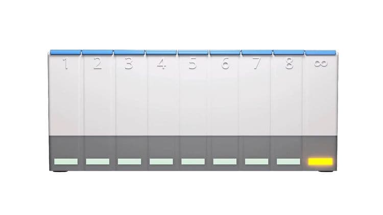 A photo of the white, grey and blue MedpeR dosette box. There is a yellowish orange light on the slot in the bottom right corner.